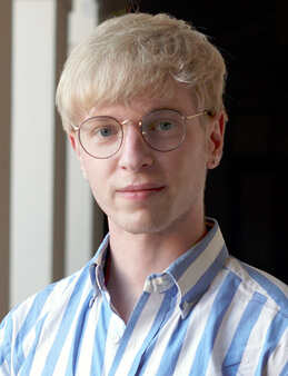 photograph of a blond person wearing a blue and white striped shirt staring into the camera.