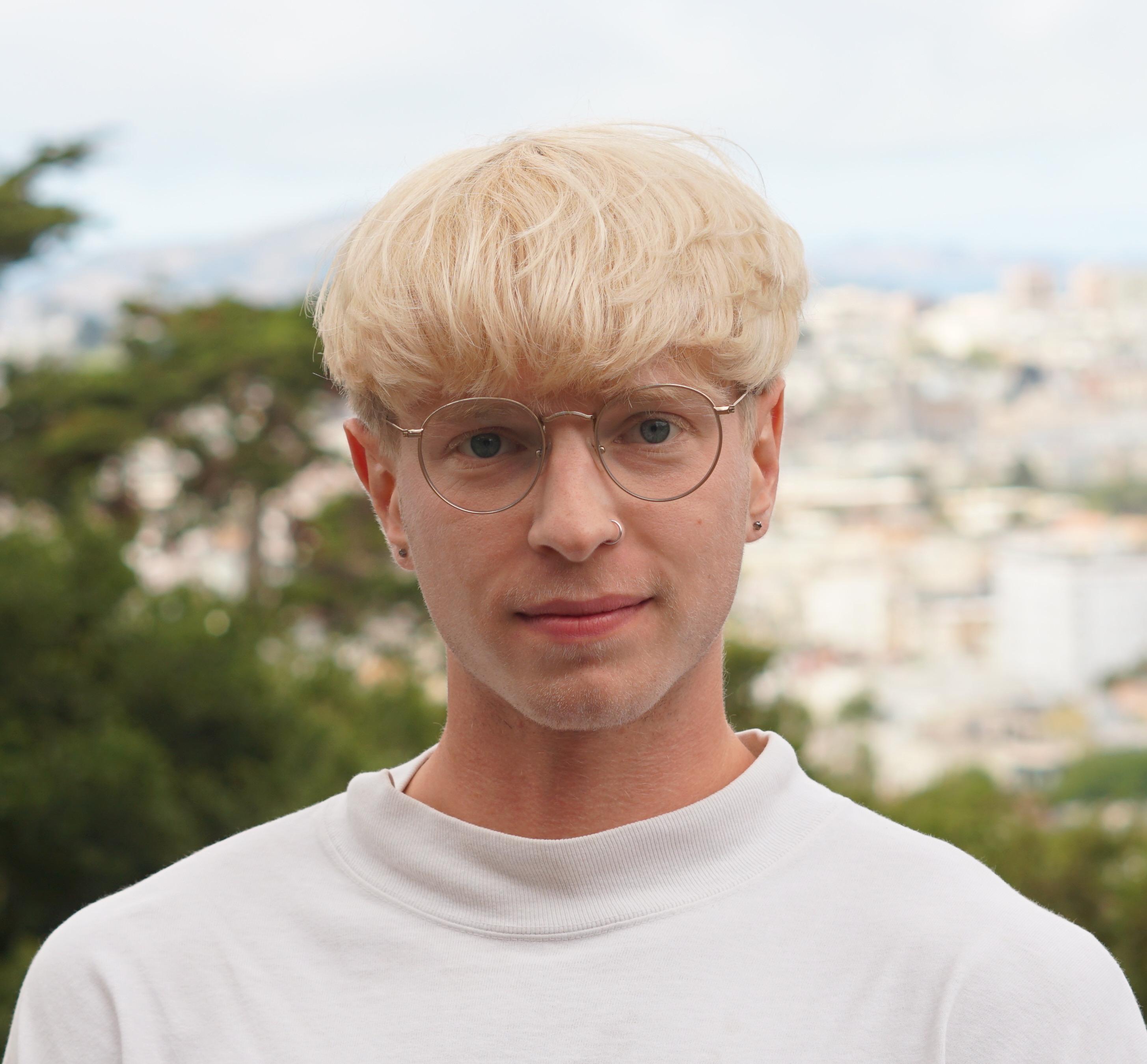 photograph of a blond person wearing wireframe glasses and a white mockneck staring into the camera.